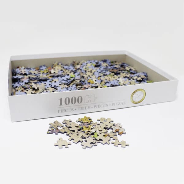 geöffnete Puzzle-Box mit durchgemischten Puzzle-Teilen, davor ein kleiner Haufen Puzzle-Teile